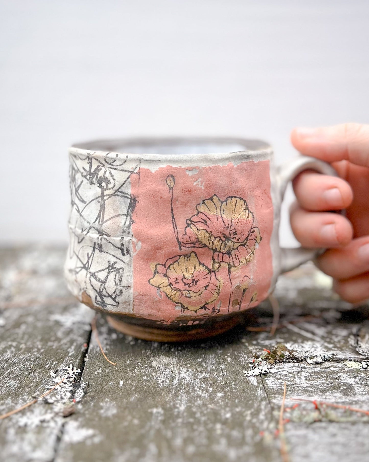 Hand holding a ceramic mug with floral design on a wooden surface