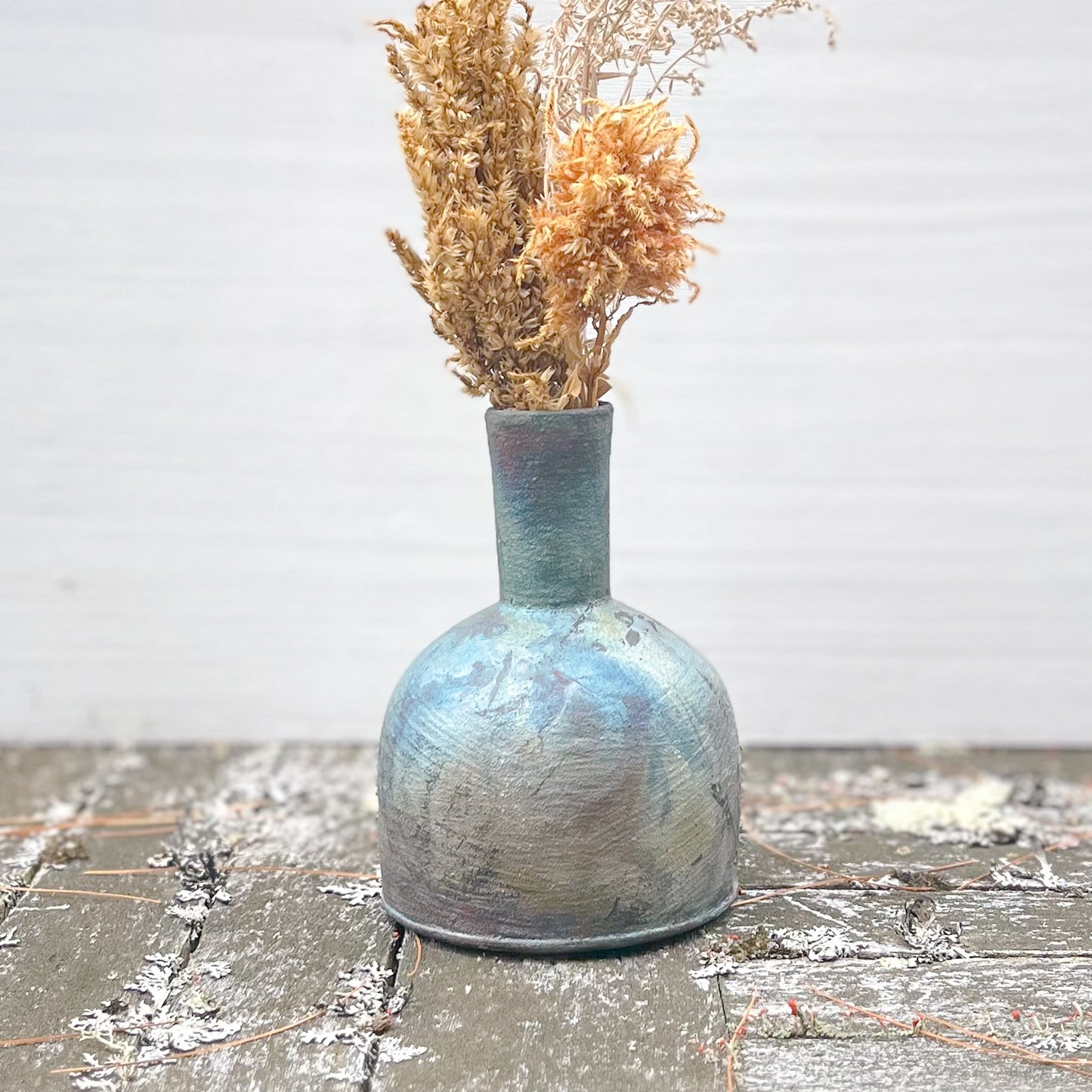 Ceramic vase with textured surface holding dried flowers on a wooden surface.
