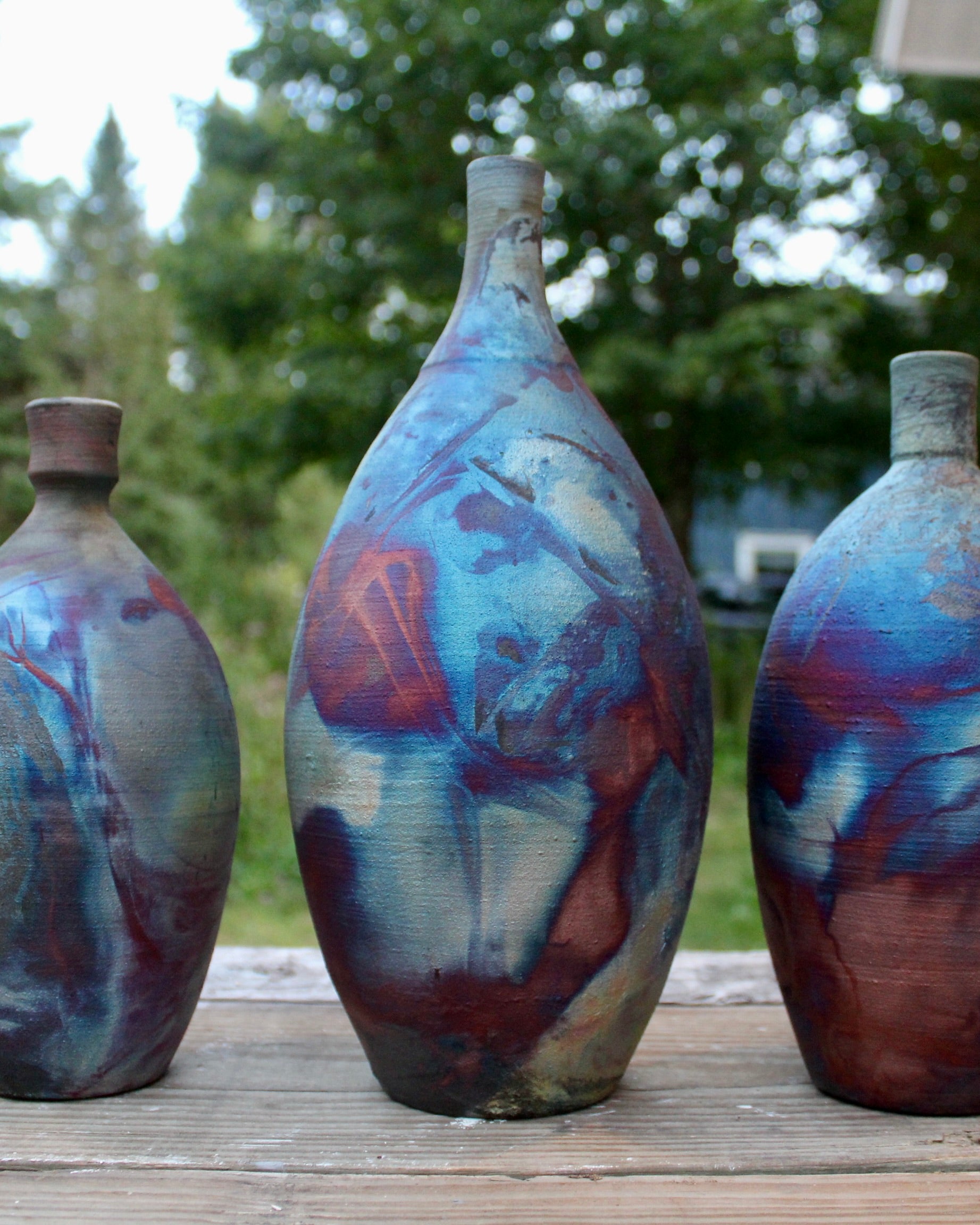 Three ceramic vases with abstract multicolor designs on a wooden surface outdoors.