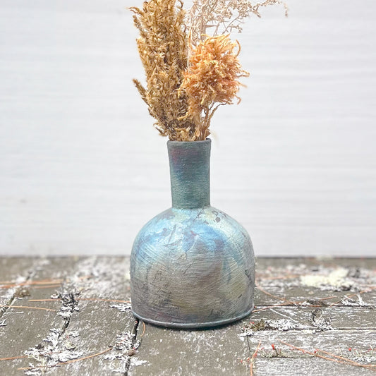 Ceramic vase with textured surface holding dried flowers on a wooden surface.